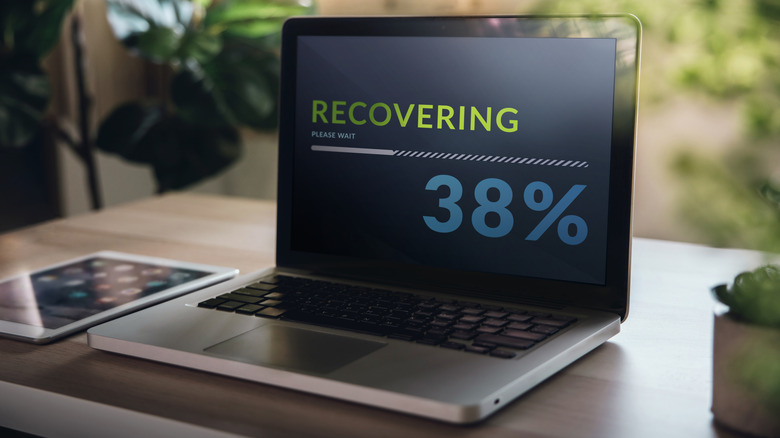 A laptop showing recovery progress on screen, sitting on a table next to an iPad