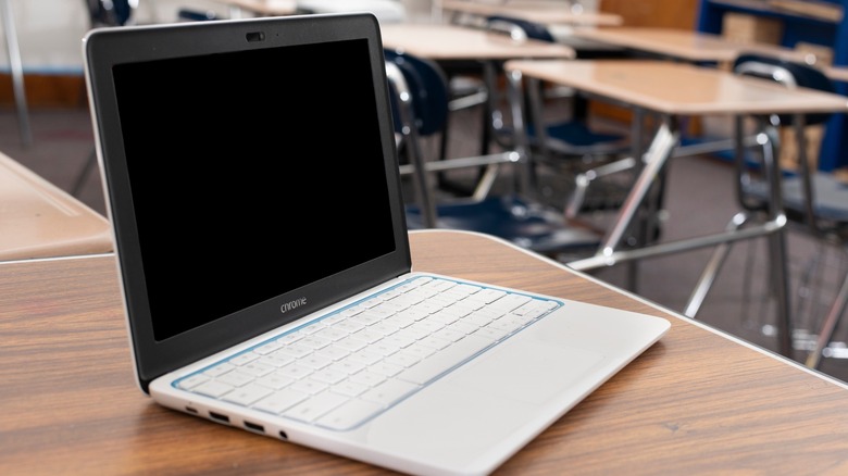 Powqered off Chromebook sitting on desk in a classroom.