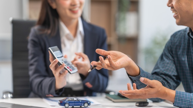 A woman holds out a calculator in front of a man during a conversation in a corporate setting