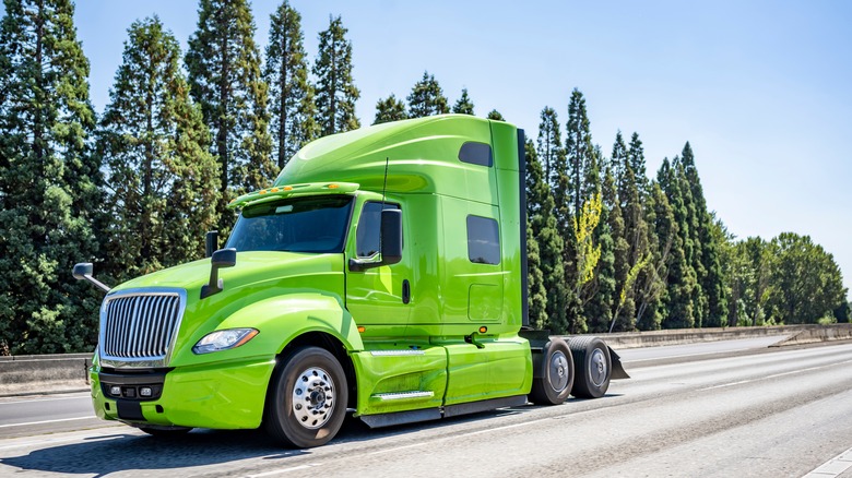 Green semi-truck driving down road