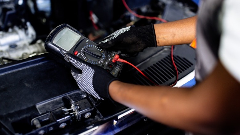 A person using a multimeter to diagnose a car electrical problem