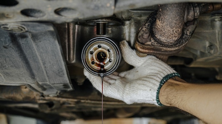 A mechanic removing an old engine oil filter with what appears to be very dirty oil