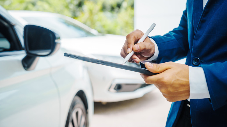 A person writing on a tablet in front of two cars.