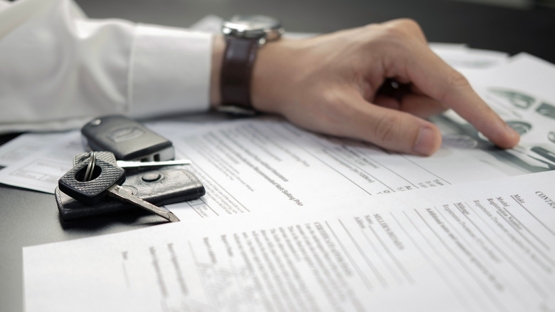 A person looking over car-related documents, with keys on the table.