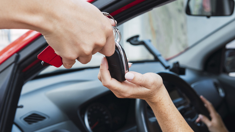 A person in a car being handed keys by someone outside.