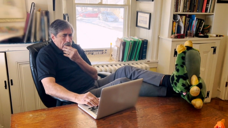 Don Lessem looks at a laptop computer while wearing dinosaur slippers