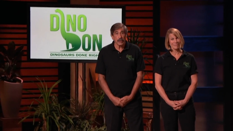 Don Lessem and Val Jones stand next to the Dino Don logo on Shark Tank