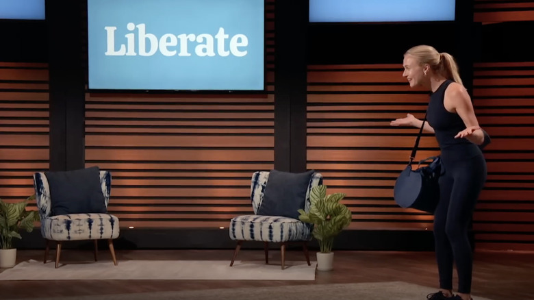 Liberate founder Olivia Bowser standing on the set of 'Shark Tank" wearing an all-black workout outfit and carrying a gym bag