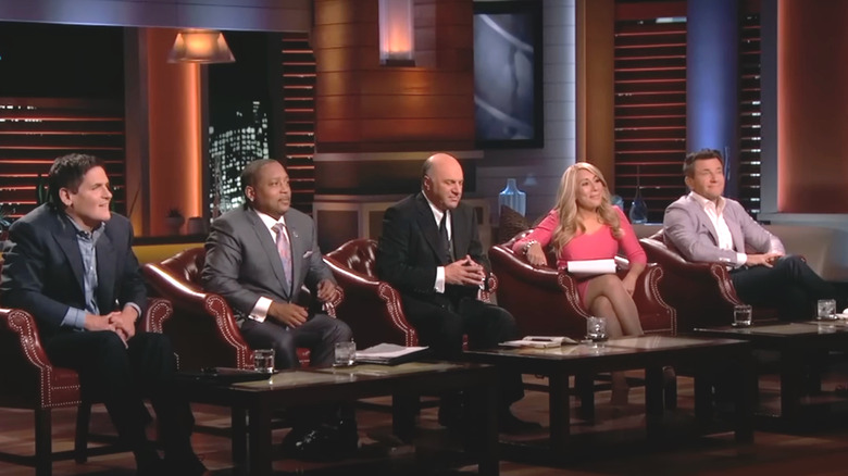 Mark Cuban, Daymond John, Kevin O'Leary, Lori Greiner, and Robert Herjavec sitting in a row while listening to a presentation on Shark Tank