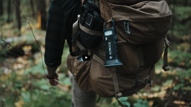 hiker in woods with X torch flashlight clipped to backpack