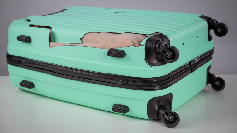 A Damaged Mint Colored Suitcase Laying Flat On The Ground