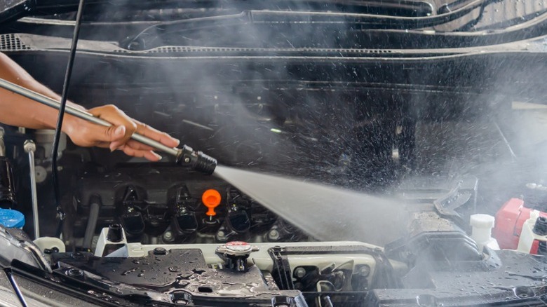 A person using a pressure washer to clean their engine bay