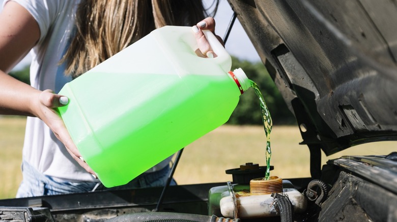 A person adding green coolant to their engine's coolant reservoir