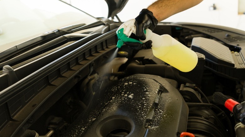 A person using a spray bottle to clean an engine bay