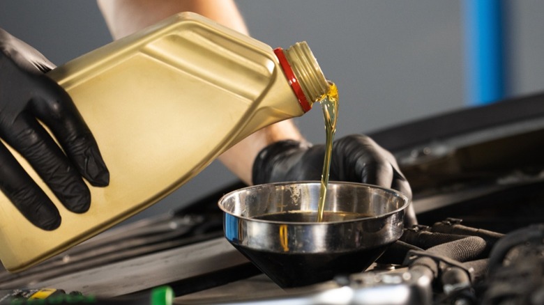 Gloved hand pouring engine oil into a car