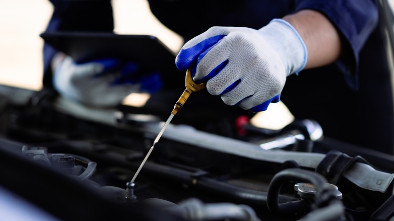 A gloved hand checking the engine oil level