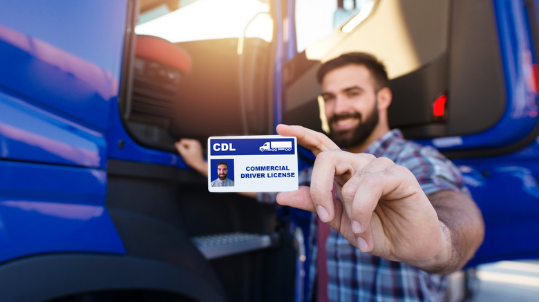 A man holds up a sample commercial driver's license at the side of a truck