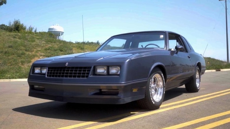 1983 Chevrolet Monte Carlo SS parked on road with a grassy hill and a water tower in the background