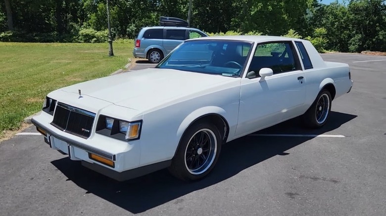 White 1986 Buick Regal T-Type Turbo parked on an asphalt surface with trees and a minivan in the background