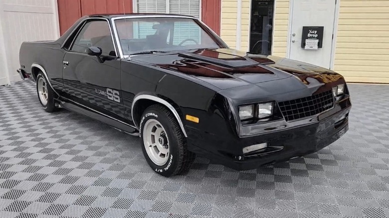 Front 3/4 shot of a Black 1984 El Camino SS Choo Choo Custom parked outside yellow house