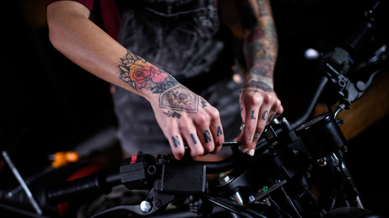 Person with tattoos working on motorcycle