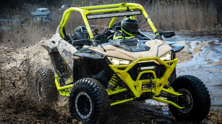 A yellow utility task vehicle, also known as a UTV or side-by-side, carrying two passengers.