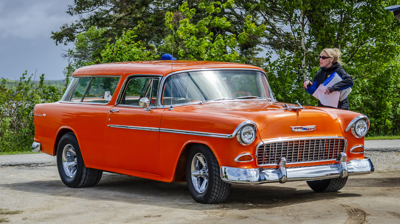 Red 1955 Chevy Nomad parked near trees on a cloudy day