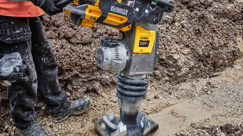 A person using a DeWalt Powershift rammer on dirt.