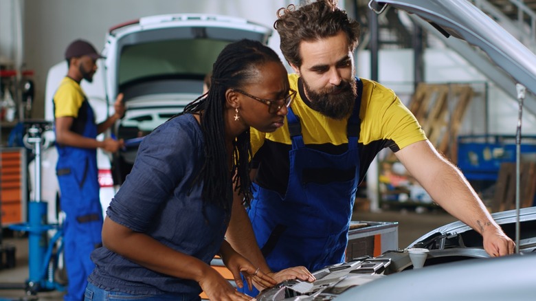 A technician showing a customer under the hood of the car