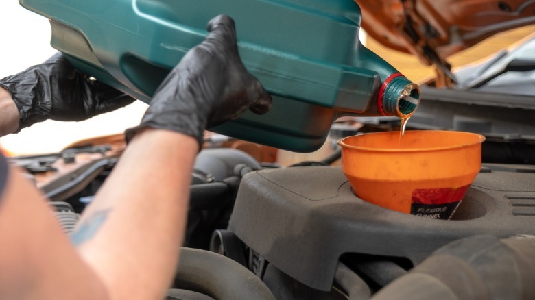 A person adding fresh oil to their engine using an orange funnel