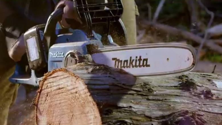 Person using Makita X2 chainsaw to cut a log