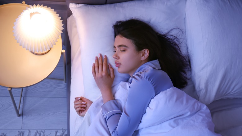 Woman sleeping with light on next to her bed