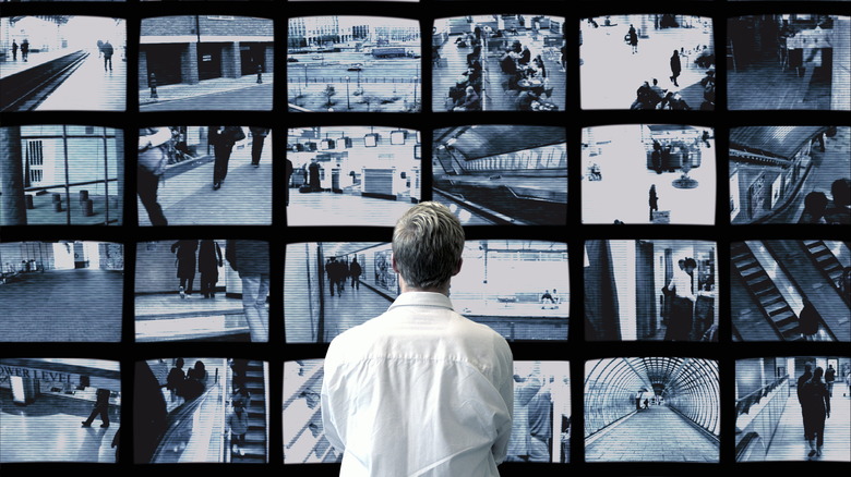 A man stands before a bank of surveillance feeds on a wall of mounted displays