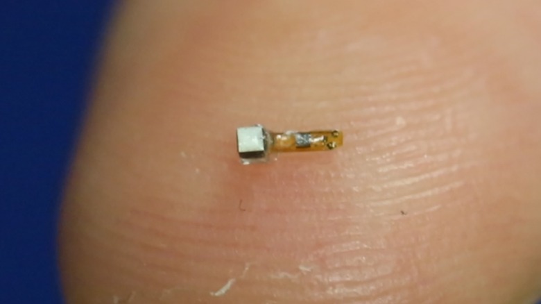 A tiny smart dust machine resting on a person's finger