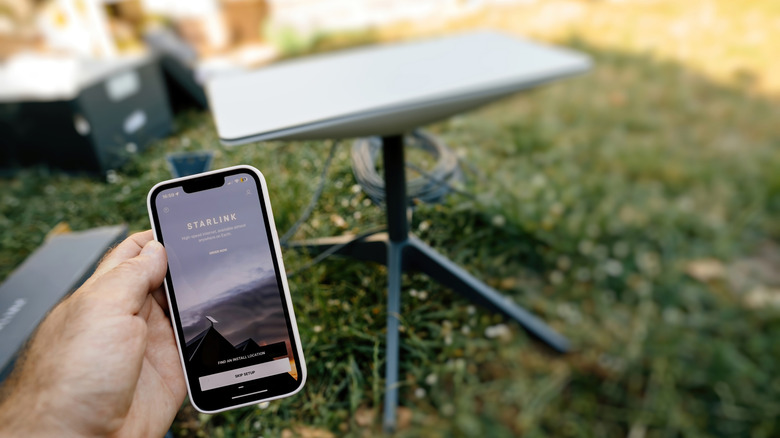 Hand holding a phone showing the Starlink app and the Starlink dish in the background