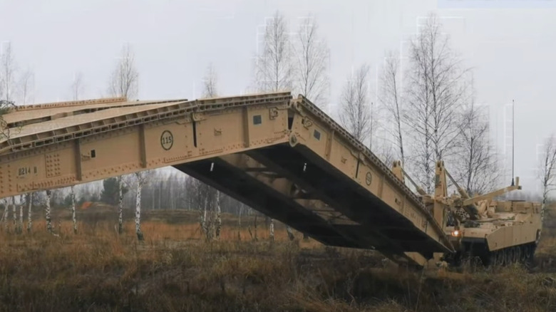 A tan colored Army bridgelayer laying a bridge