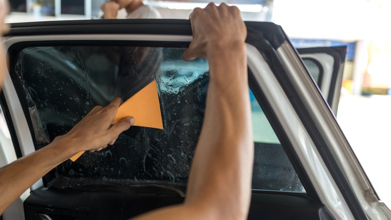 A person installs dark window tint on a vehicle's rear right-side door.