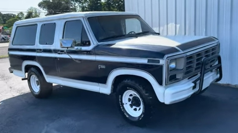 A white and black Ford B-150 parked outside.