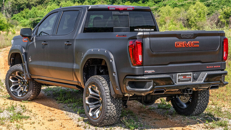 Rear view of a black GMC 1500 Limited on dirt road.