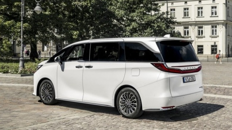 Rear 3/4 shot of a parked Lexus LM with people, trees, and buildings in the background