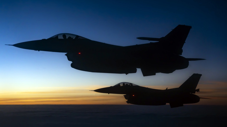 A pair of U.S. Air Force F-16 Flying Falcons aloft, with the setting sun in the background, showing only their silhouettes.