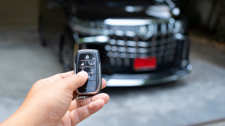 A car owner using a key fob with their car in the background.