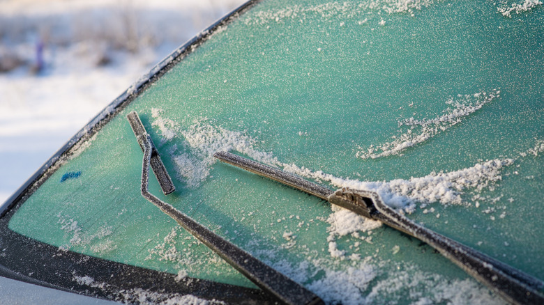 A car's windshield and wipers covered in ice and frost