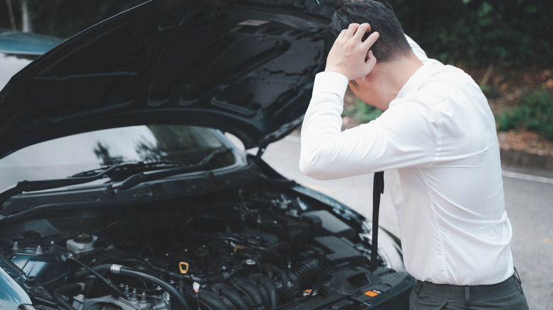 A man expressing frustration through his bodily gesture while checking the engine bay of his car