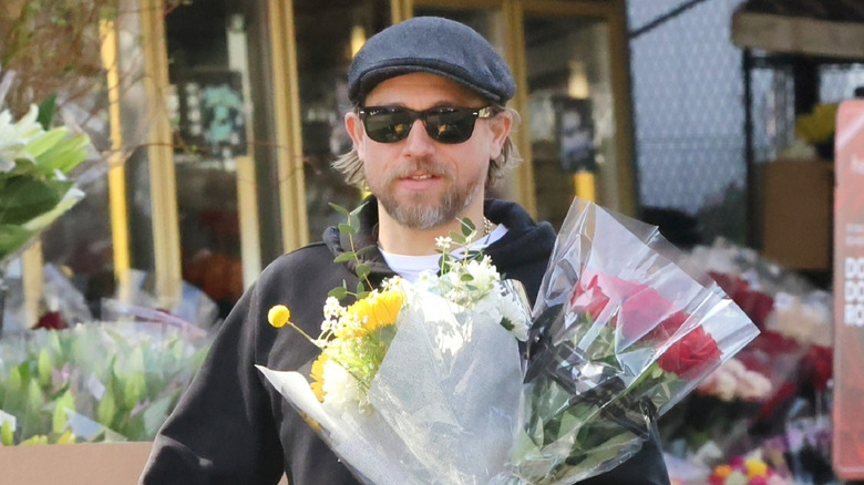 Charlie Hunnam carrying two bouquets of flowers