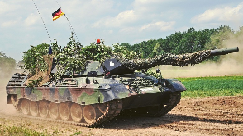 Camouflaged Leopard 1A5 with German flag on dirt road