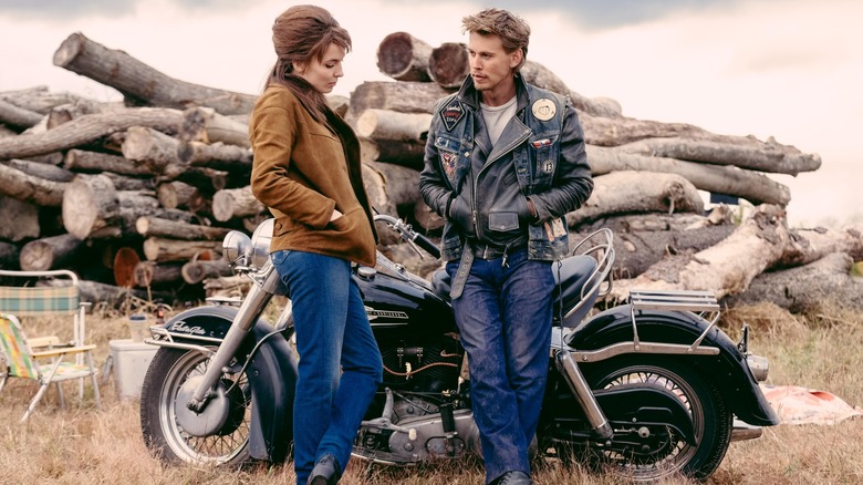 Austin Butler leaning against a motorcycle with Jodie Comer