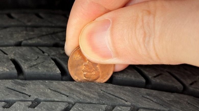 Fingers holding penny in tire tread