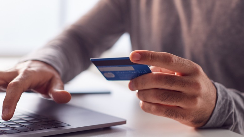 Human hand holding a card to a laptop