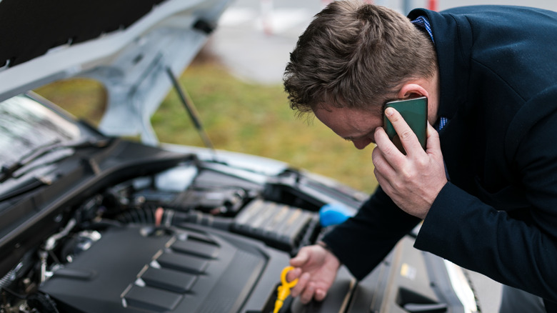 Man on phone while checking car engine